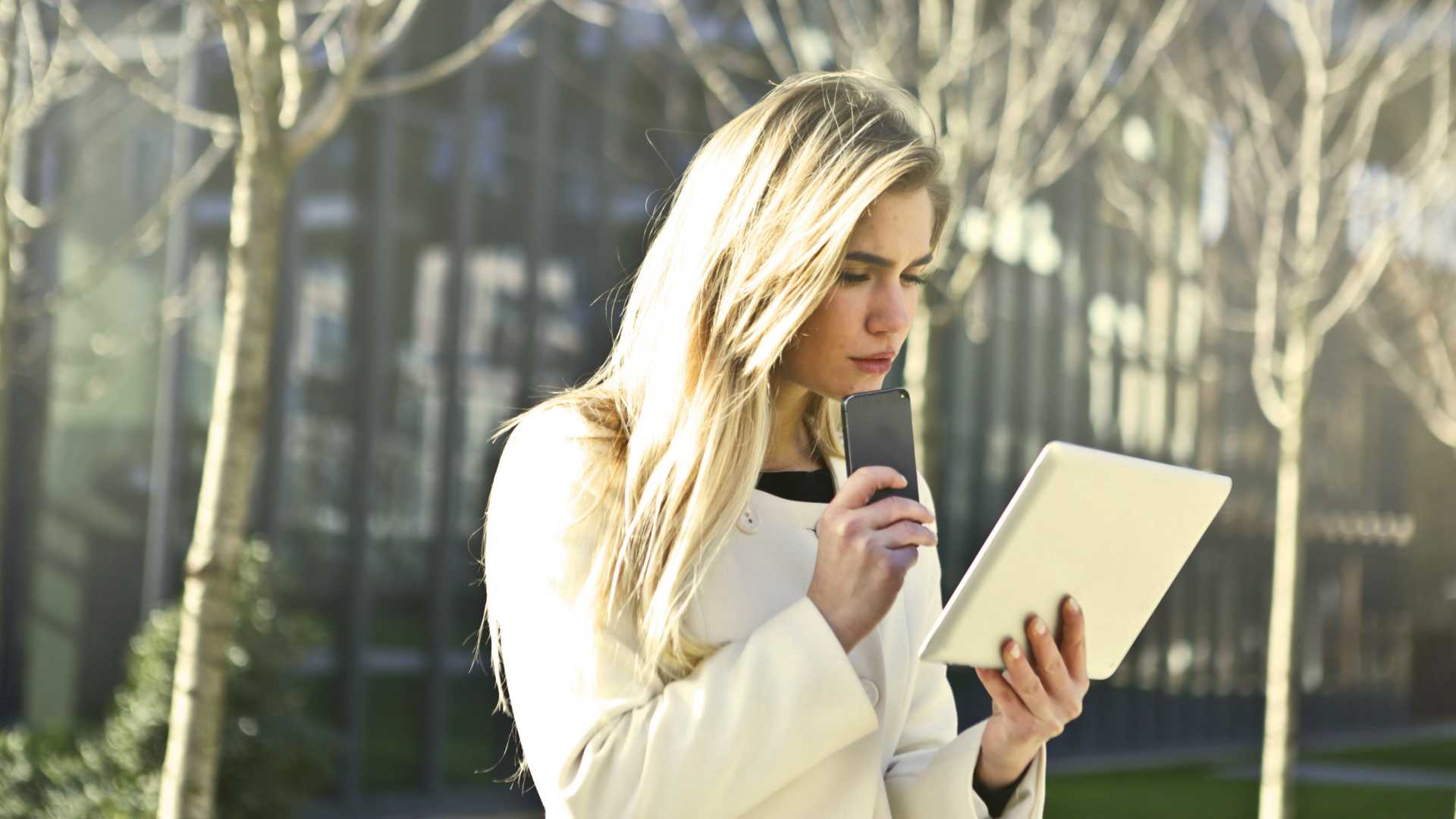 woman talking into a cell phone while looking at a tablet