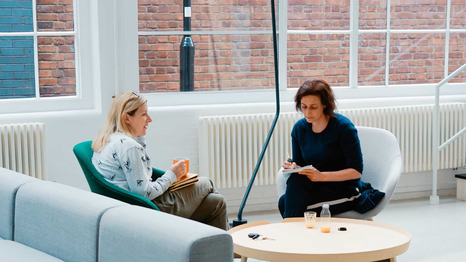 woman taking notes while listening to another woman talk