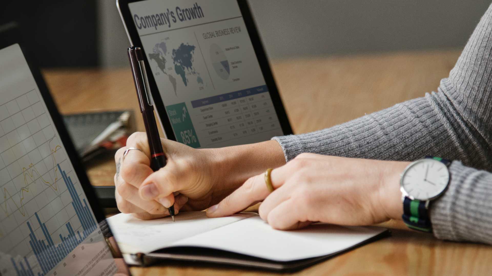 woman taking notes; company growth chart on her laptop