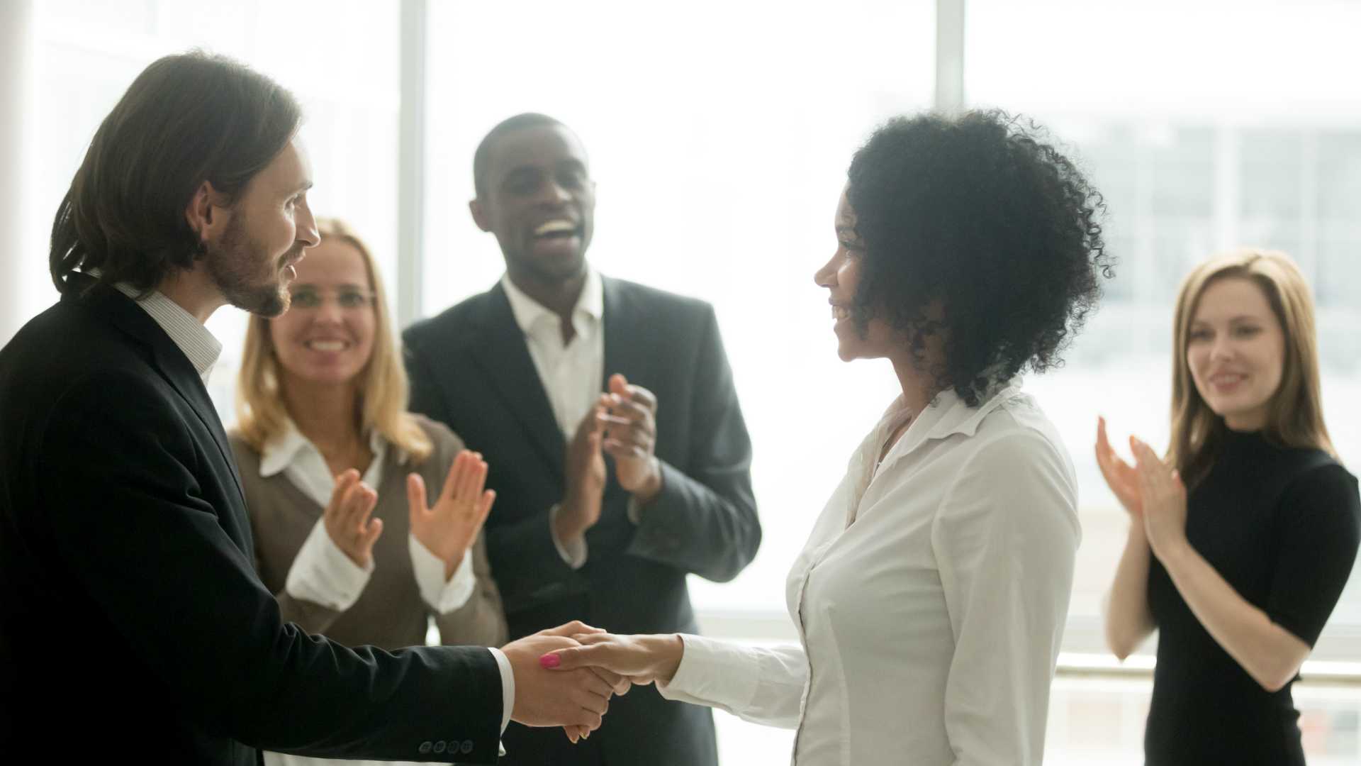 woman receiving a promotion while her team applauds