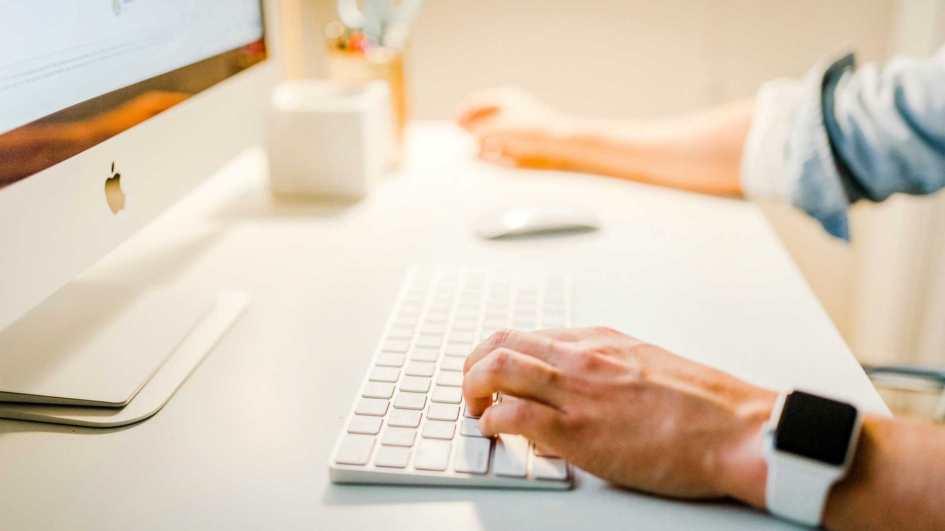 view of a man's arms with hands typing on the keyboard of a computer with a large monitor