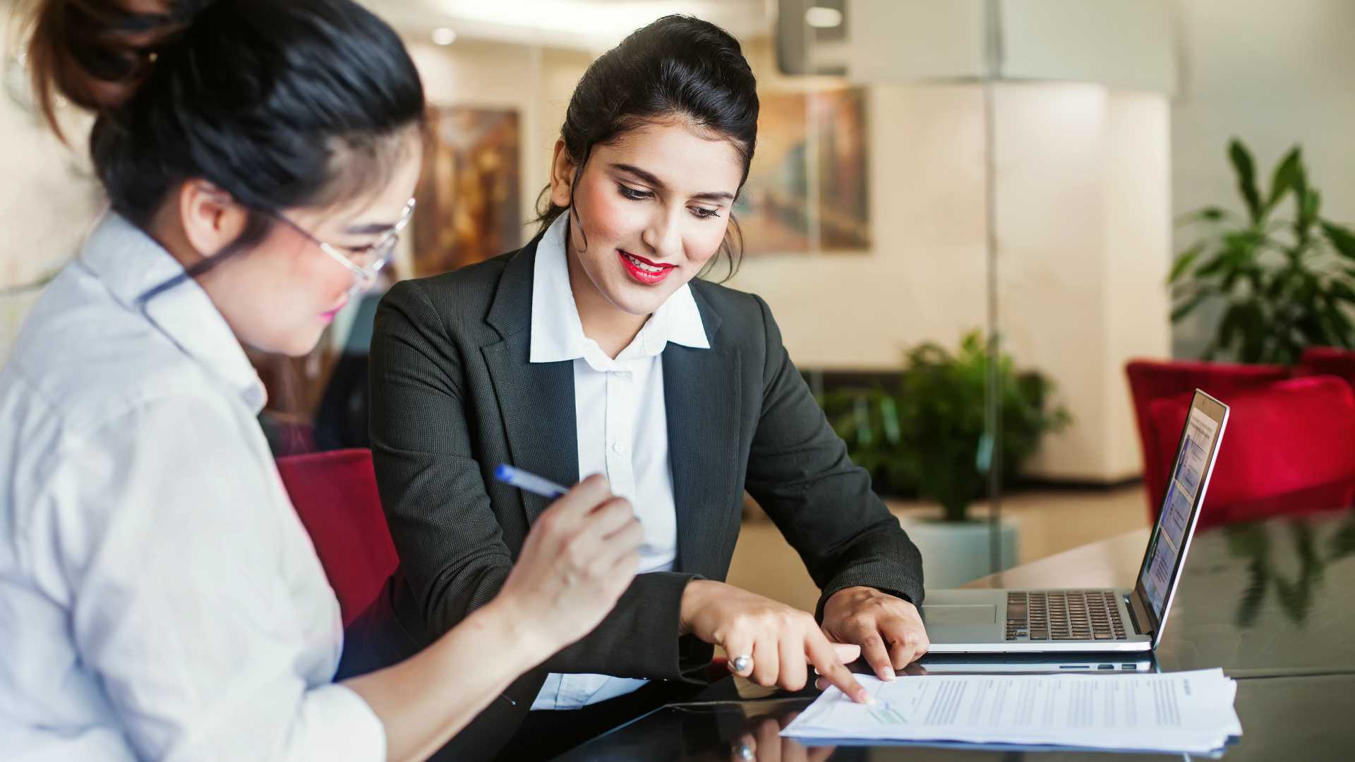 businesswoman pointing out a line in a document for another businesswoman to sign