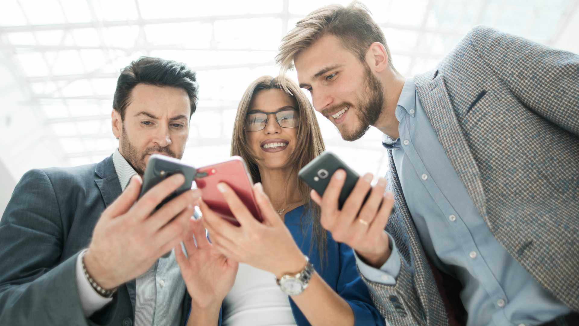 two businessmen and one businesswoman looking at each other's smartphones