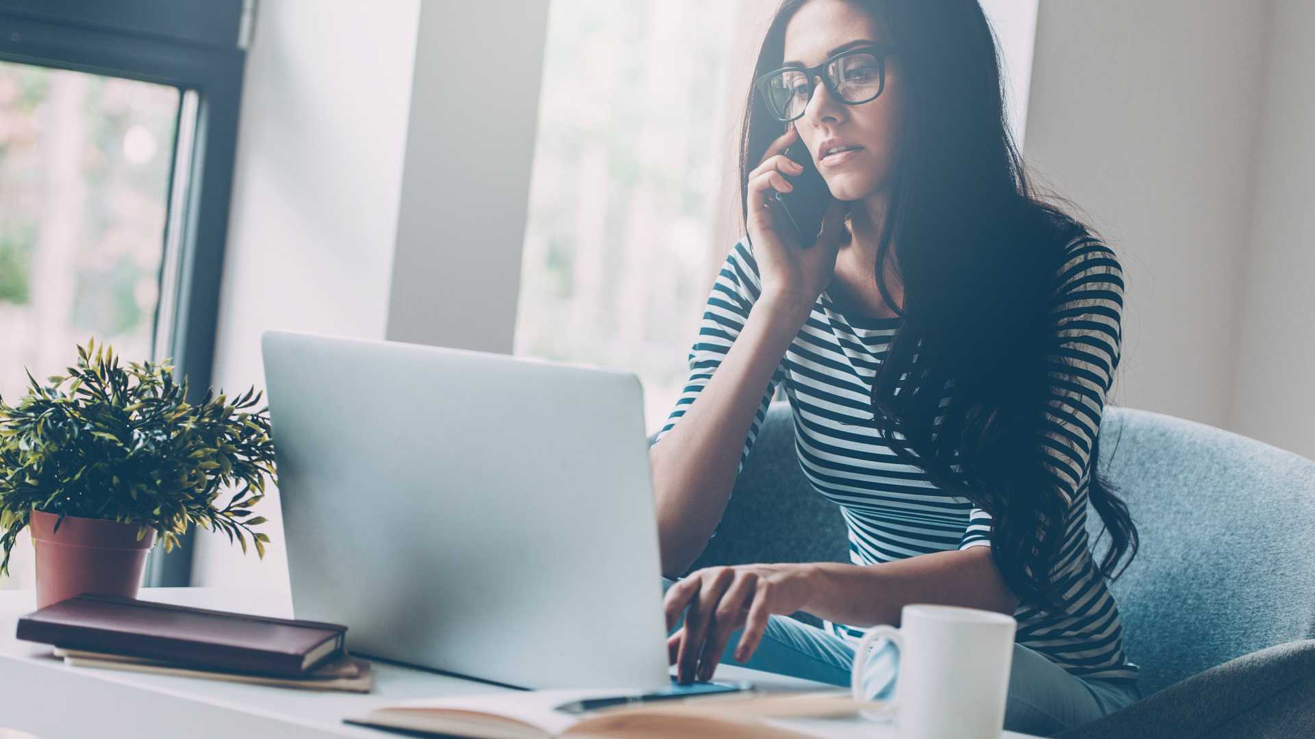 young woman on the phone and using a laptop at home or in a cafe