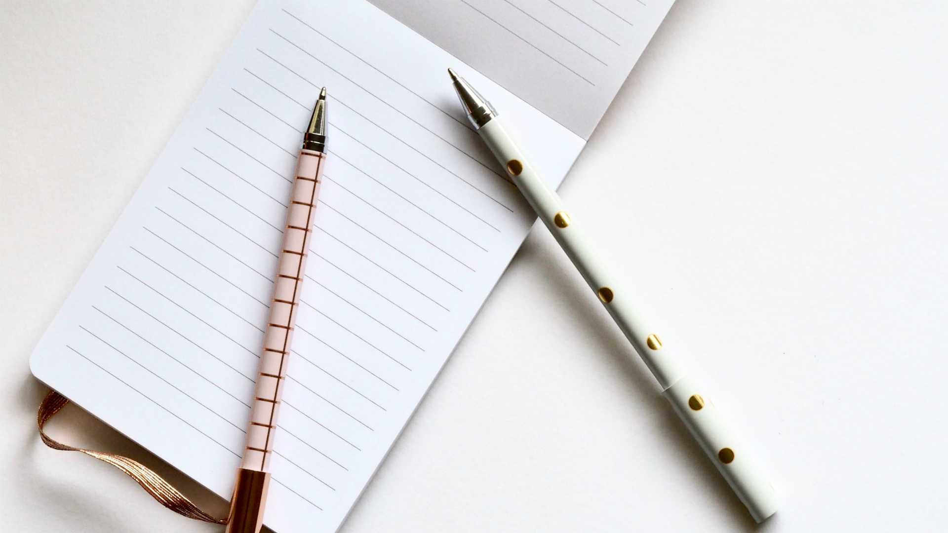 Two pens and notebook on tidy, white desk