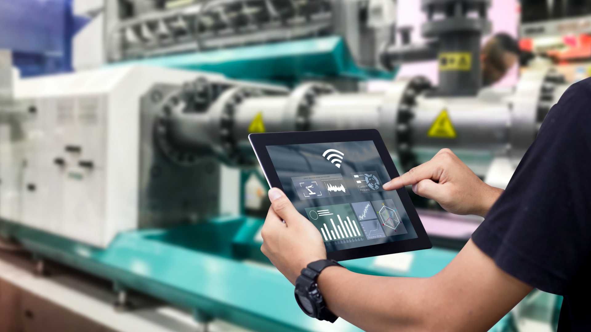 Manufacturing manager holding tablet in front of large machine while in warehouse