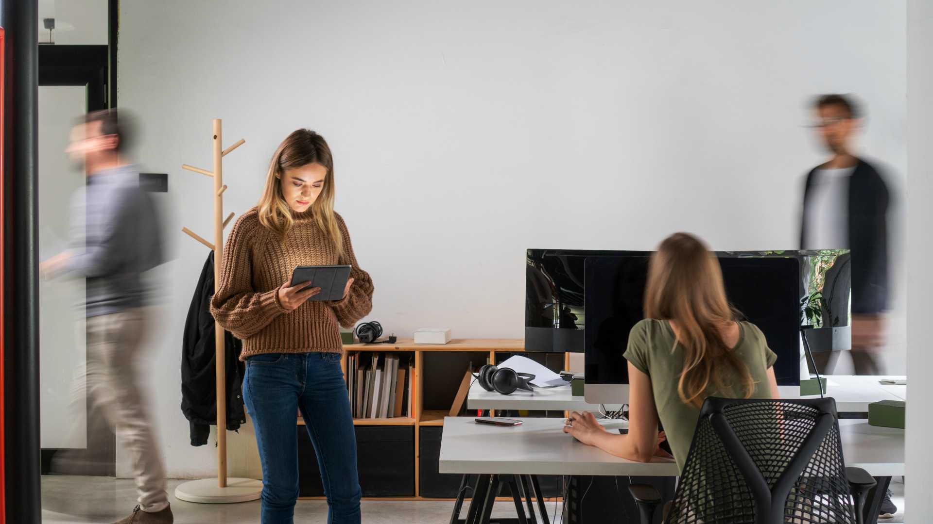 Focus on two businesswomen in modern workspace with two blurry businessman rushing through in the background