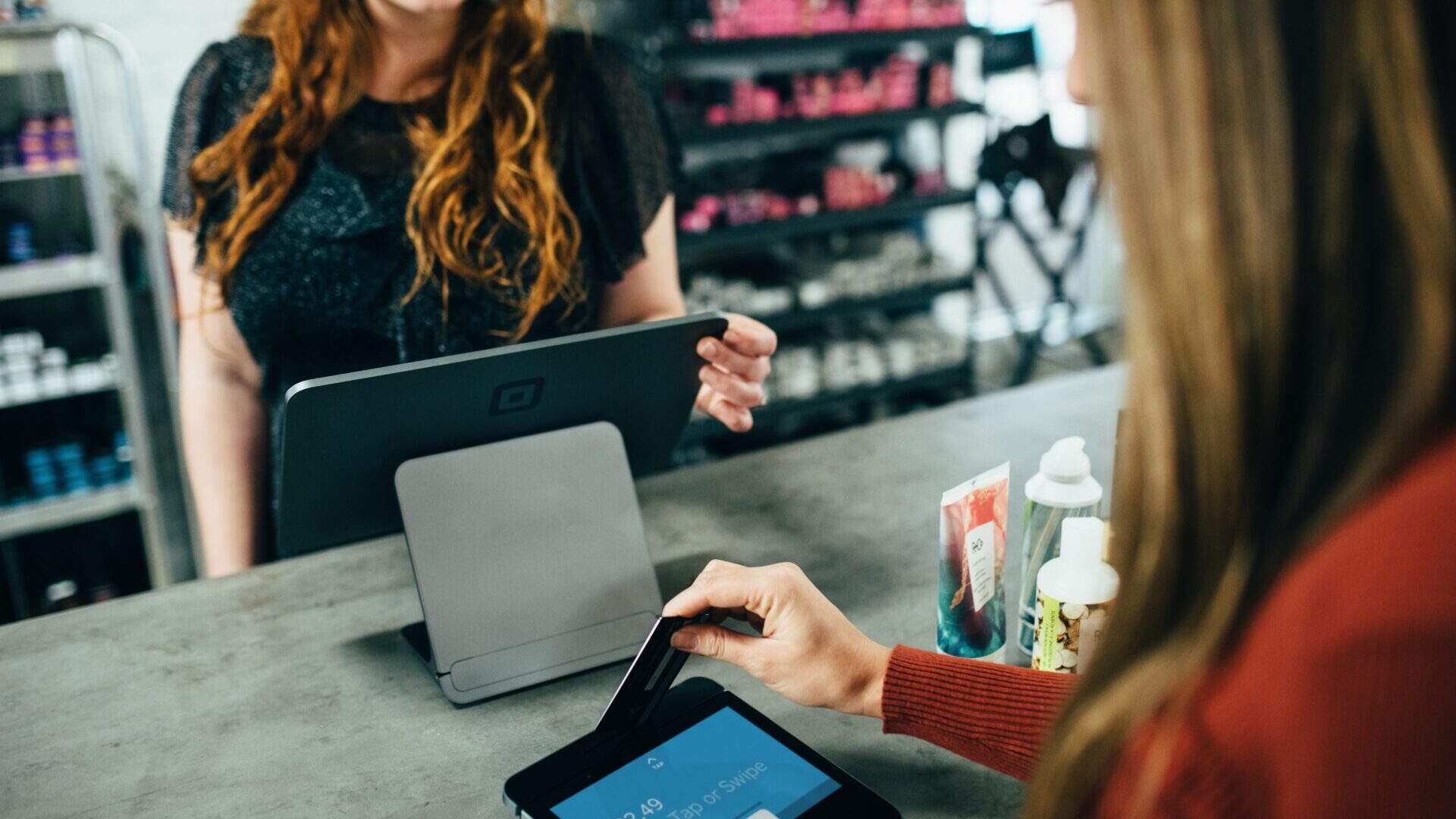 Female retail worker smiling while ringing up female customer at the cash register
