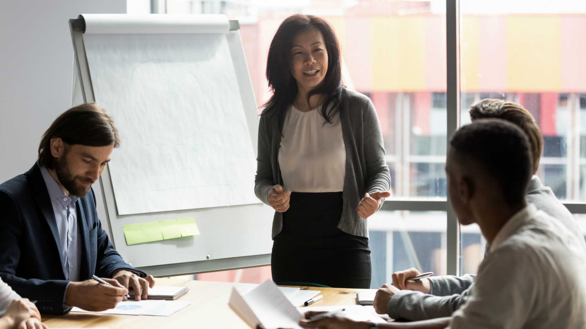 Diverse workforce listening to businesswoman colleague give presentation in board room