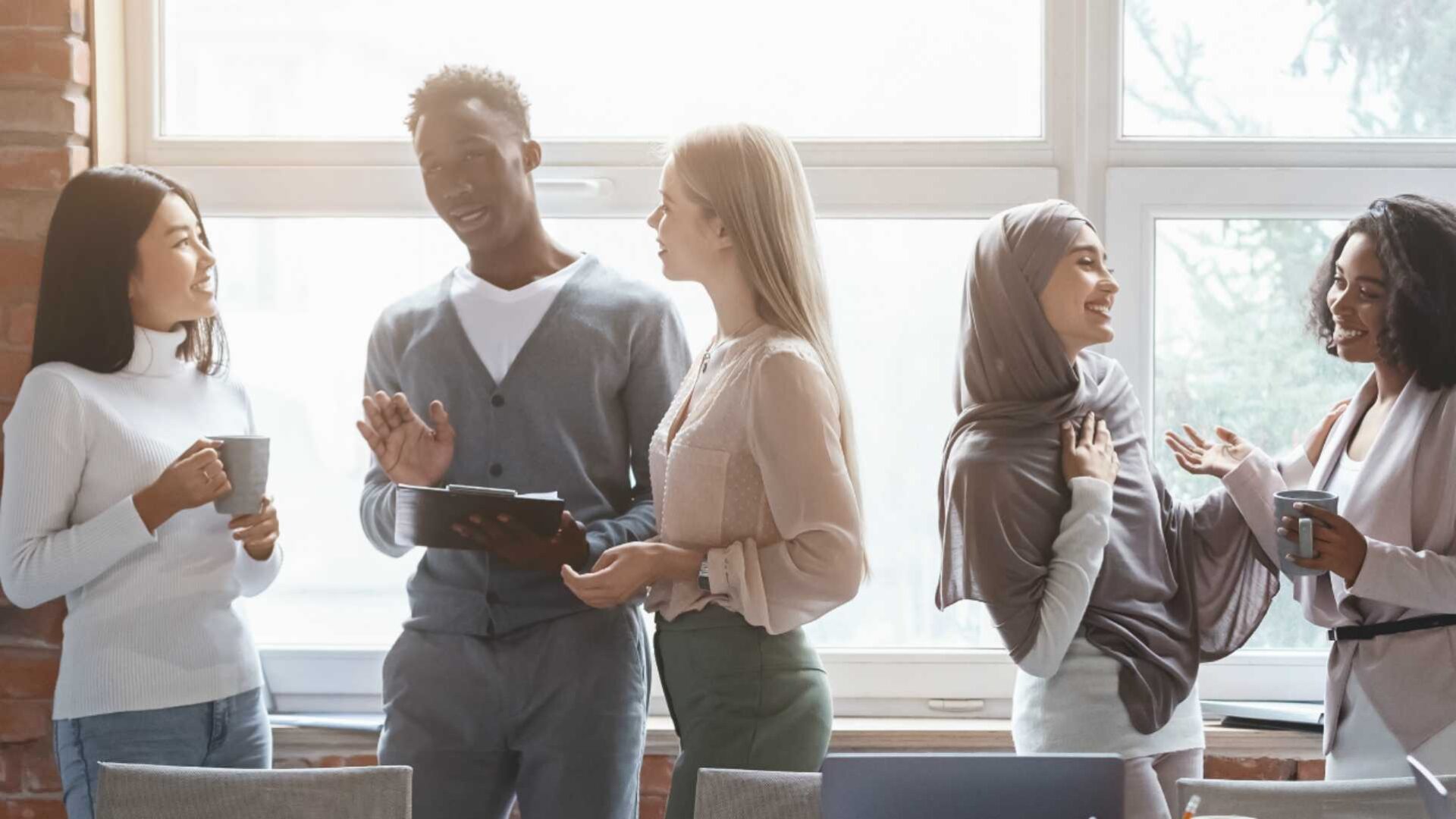 Diverse workforce collaborating and chatting in front of large window during golden hour