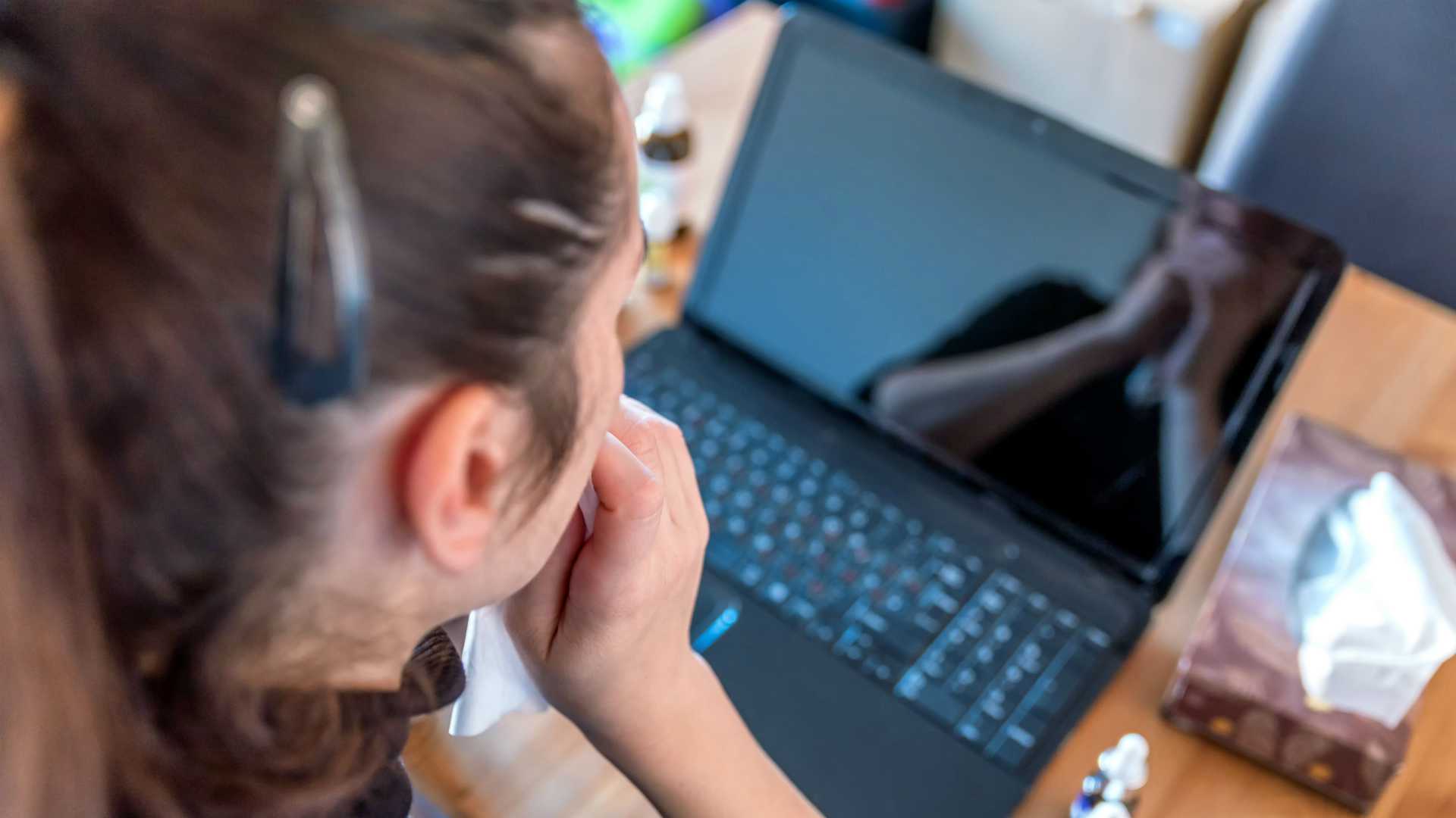 young sick woman working from home on laptop next to medicines.