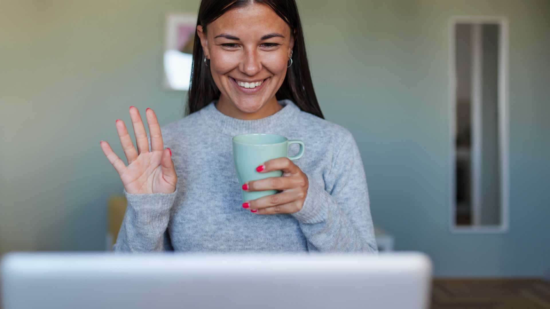 Young businesswoman working from home, joining video conference and holding cup of coffee