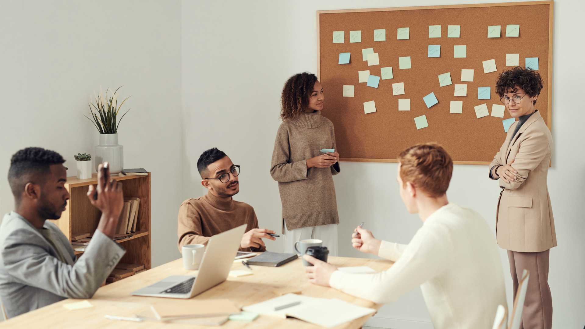 Businesswoman and team brainstorming in conference room, putting sticky notes on corkboard