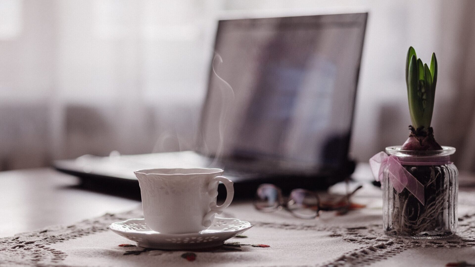 Coffee cup sitting on saucer on home office desk in front of an open laptop