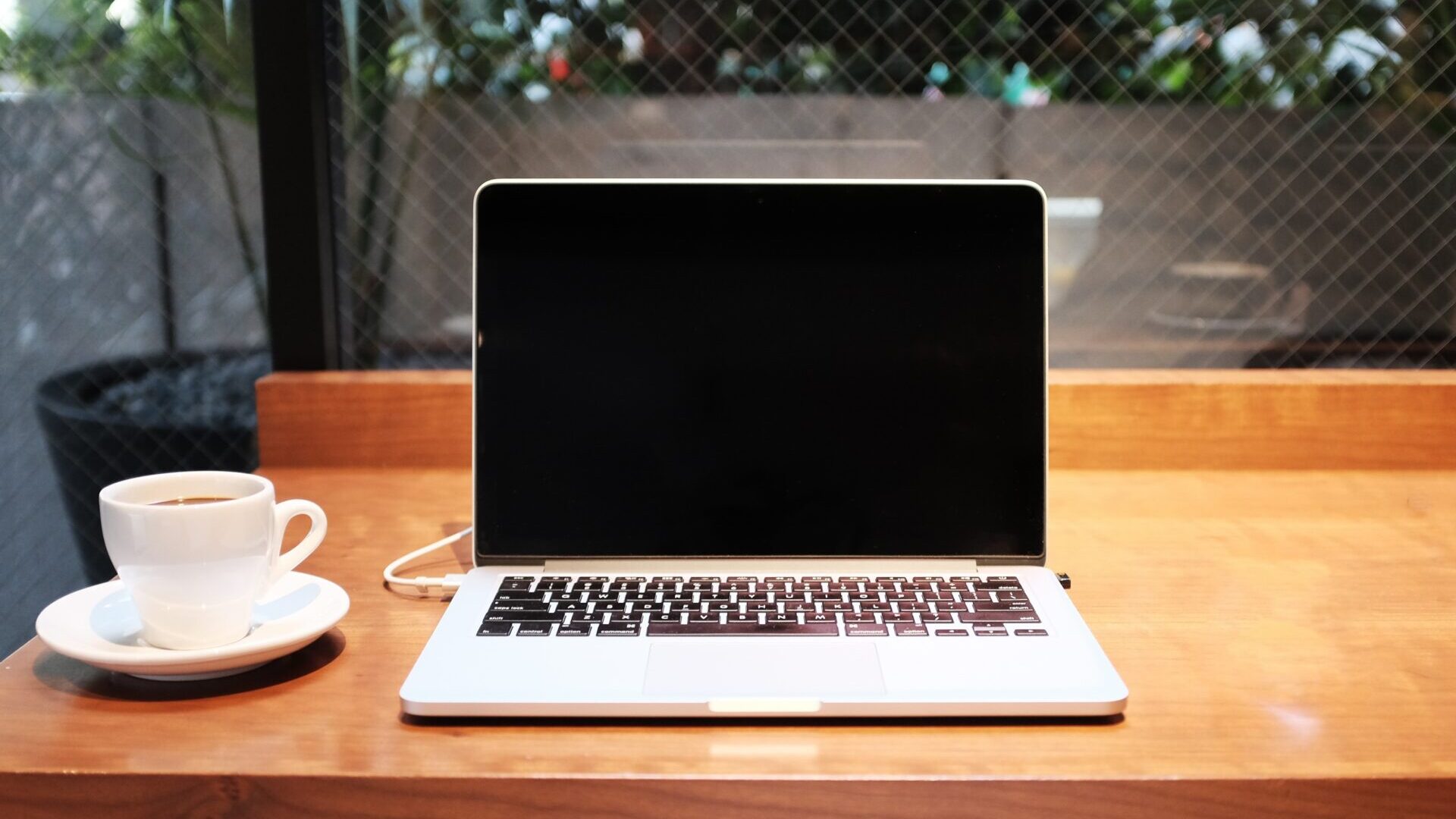 Macbook open and sitting on wooden desk next to coffee mug on saucer