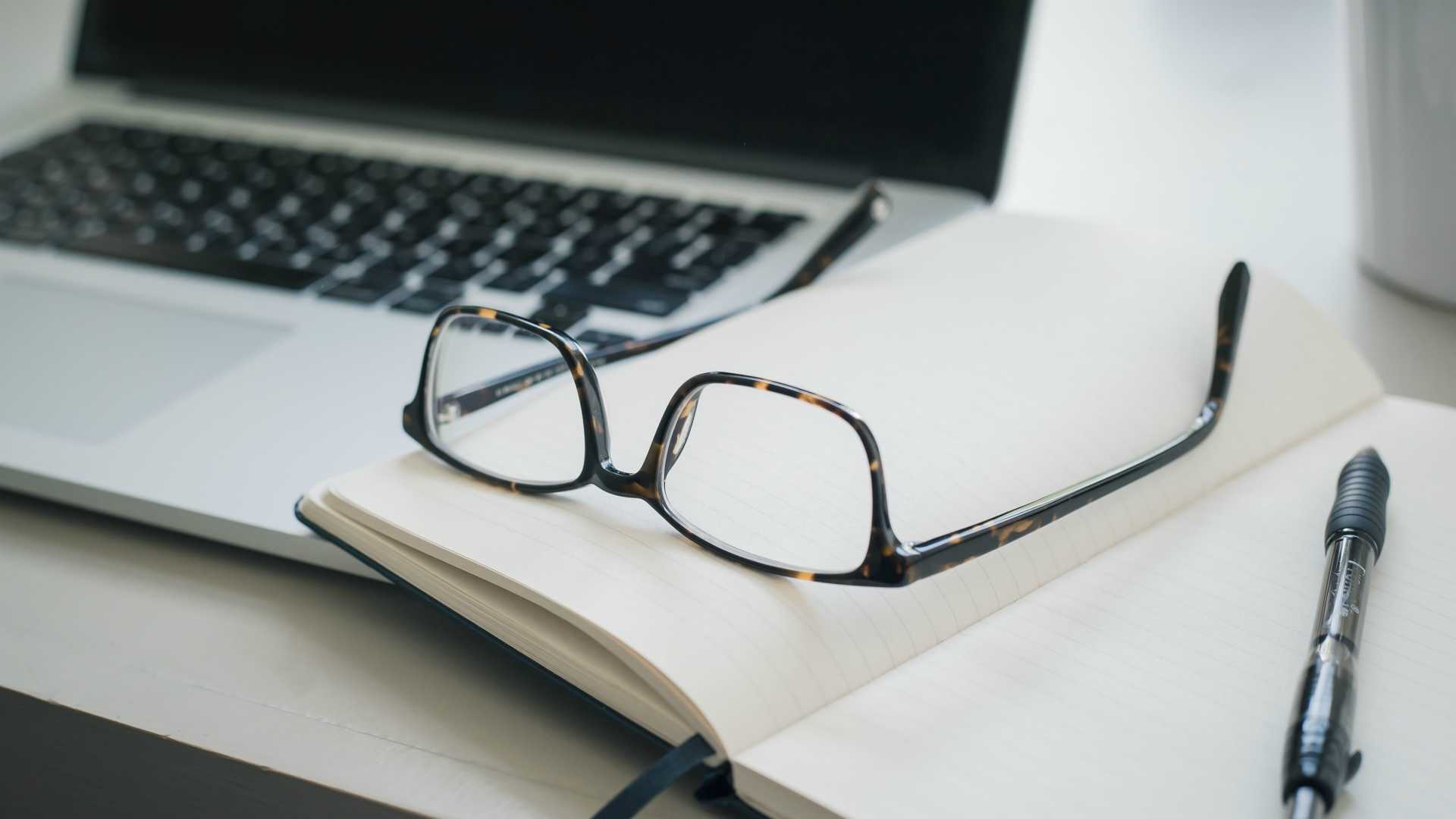 Pair of glasses sitting on open notebook with open laptop in background