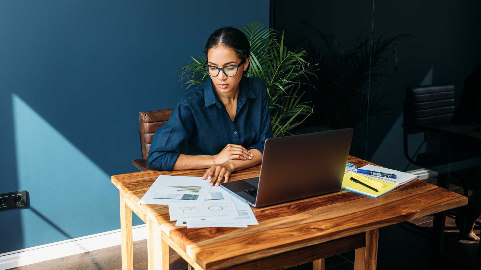 Business woman looks at charts and laptop at her desk