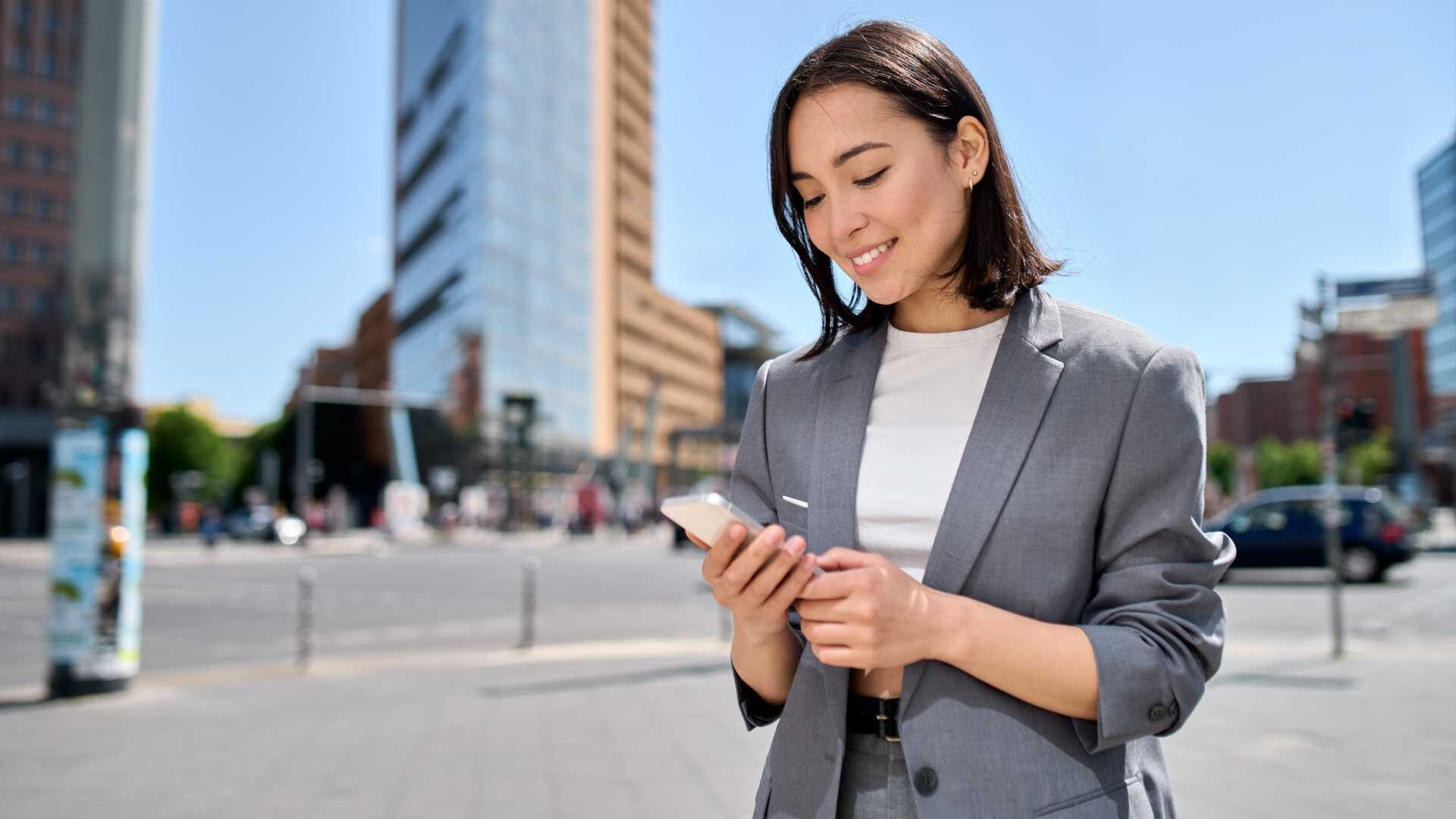 A young business woman looks at her cell phone with a cityscape in the background