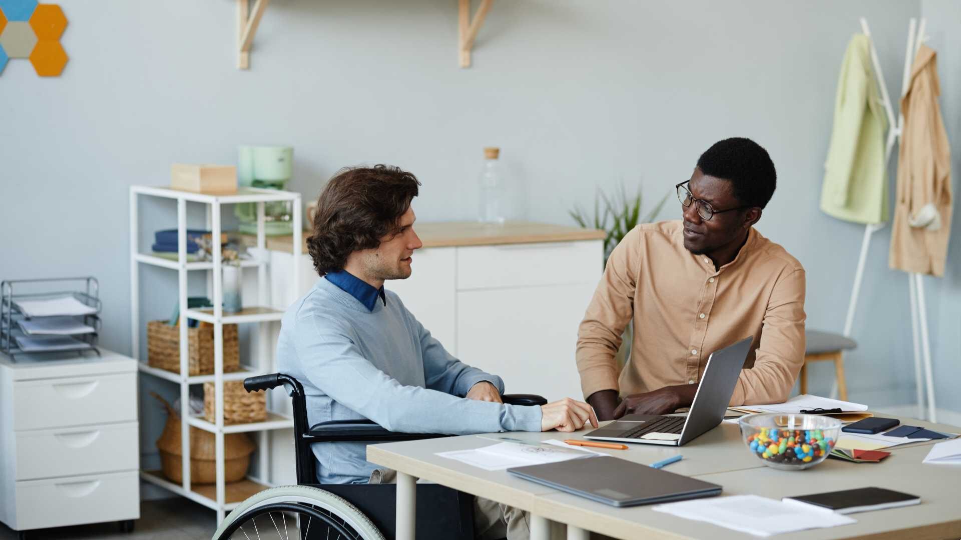 Two employees, one of whom is in a wheelchair, collaborate in an open-office setting