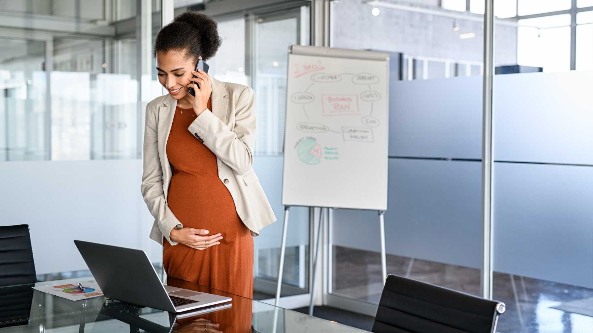 A smiling, pregnant business woman places her hand on her stomach during a virtual business meeting.