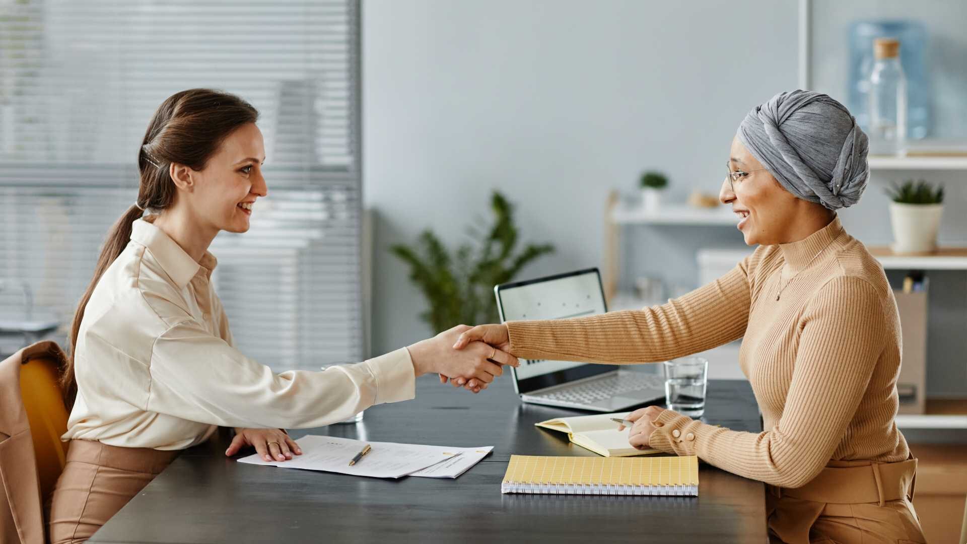Two people are sitting in an office shaking hands.