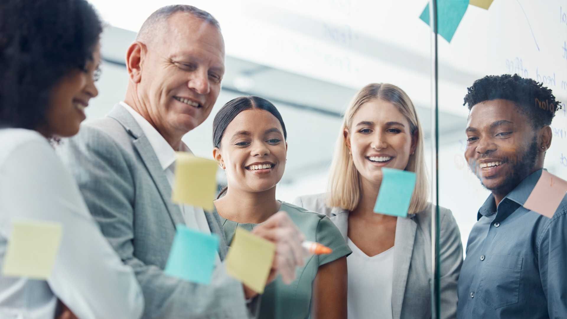 Group of work professionals huddled together by a glass wall with post-it notes.