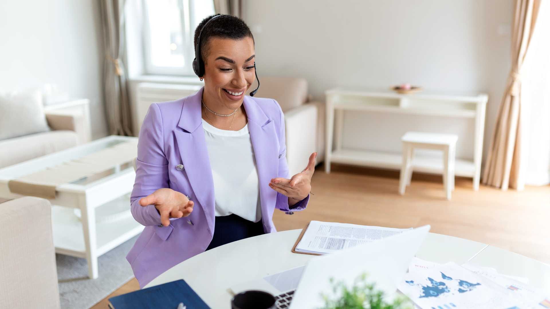 A woman wearing professional attire working from home is on a virtual meeting, wearing a headset