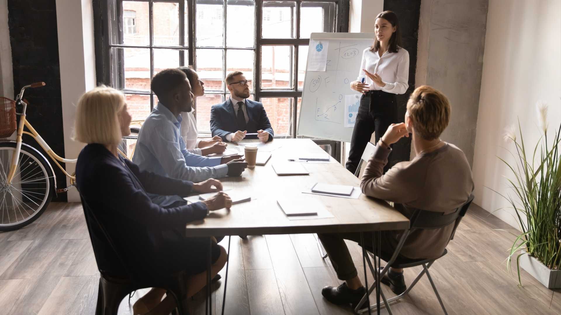 A group of employees are gathered in a conference room watching one person give a presentation