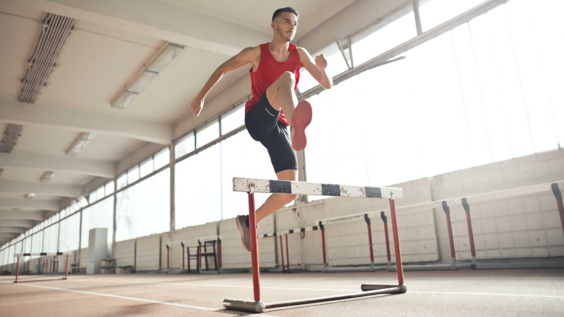 A man on an indoor track jumps over a hurdle