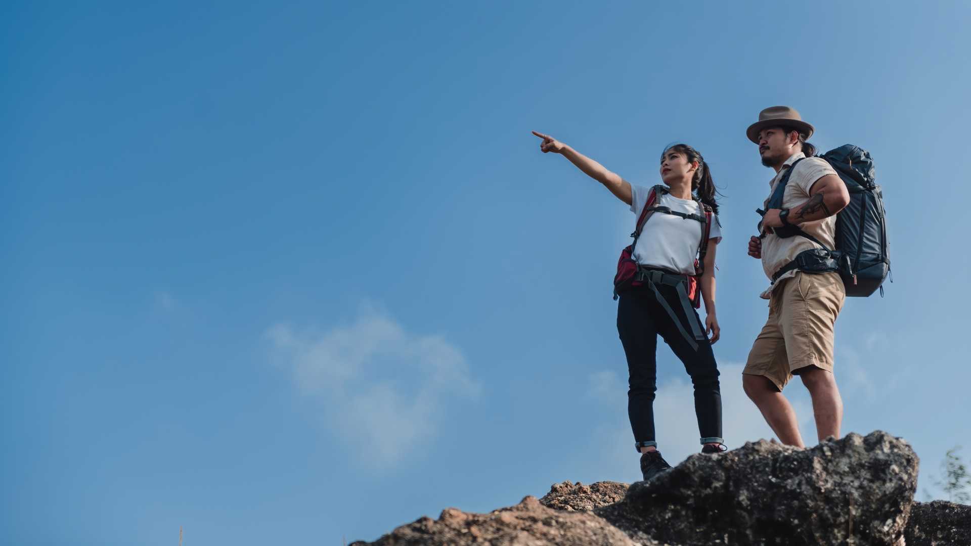 A man and a woman stand on top of a mountain looking ahead into the distance