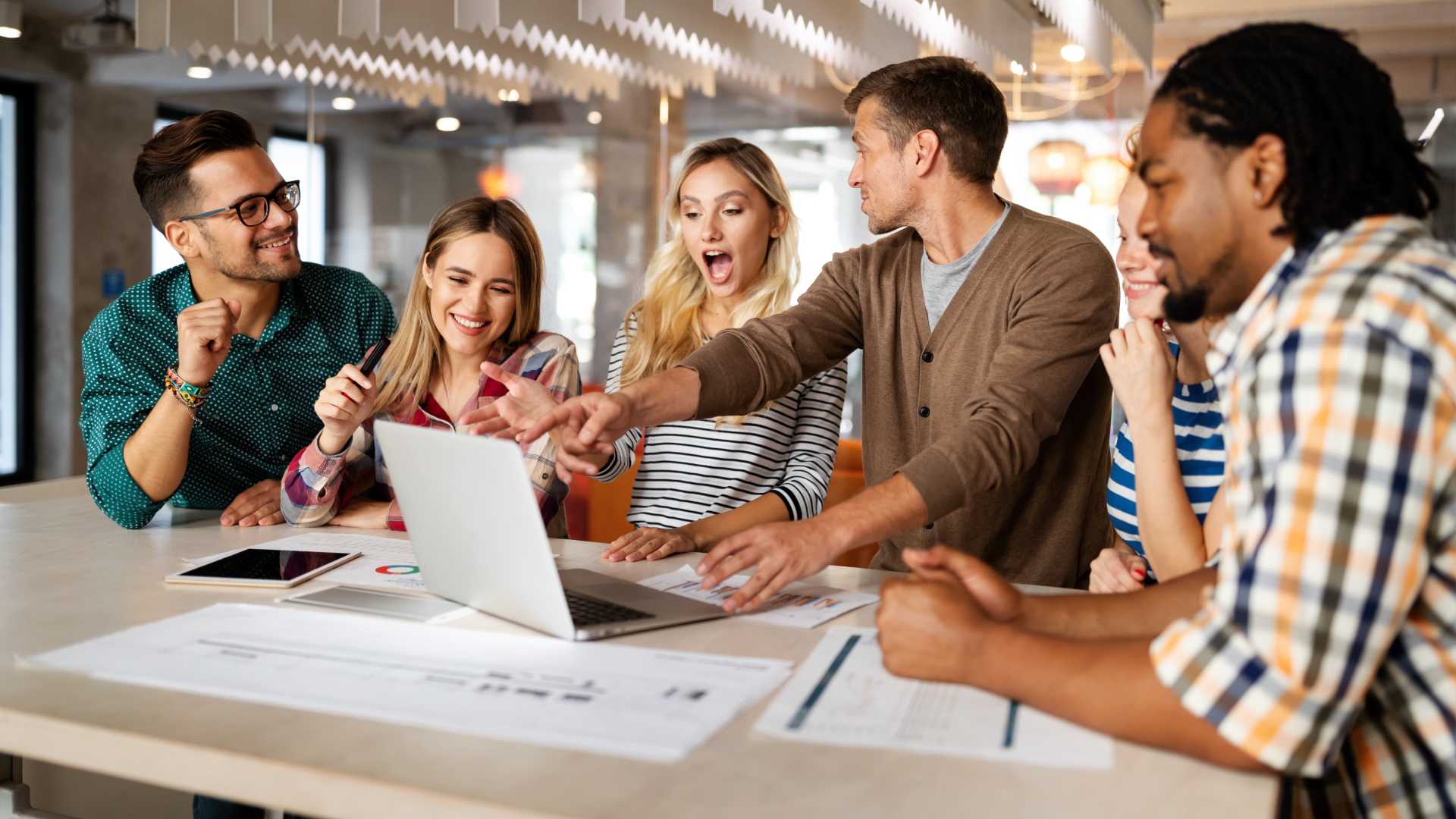A group of young professionals collaborate in an office setting while looking excited