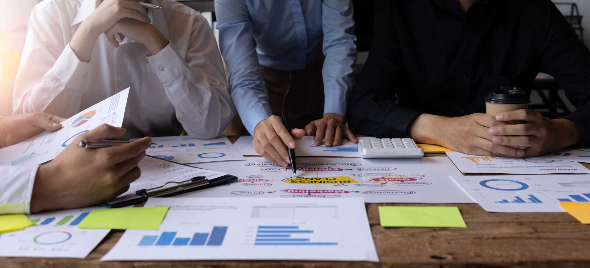 Scattered papers with charts and graphs laid out on a table in front of a group of employees