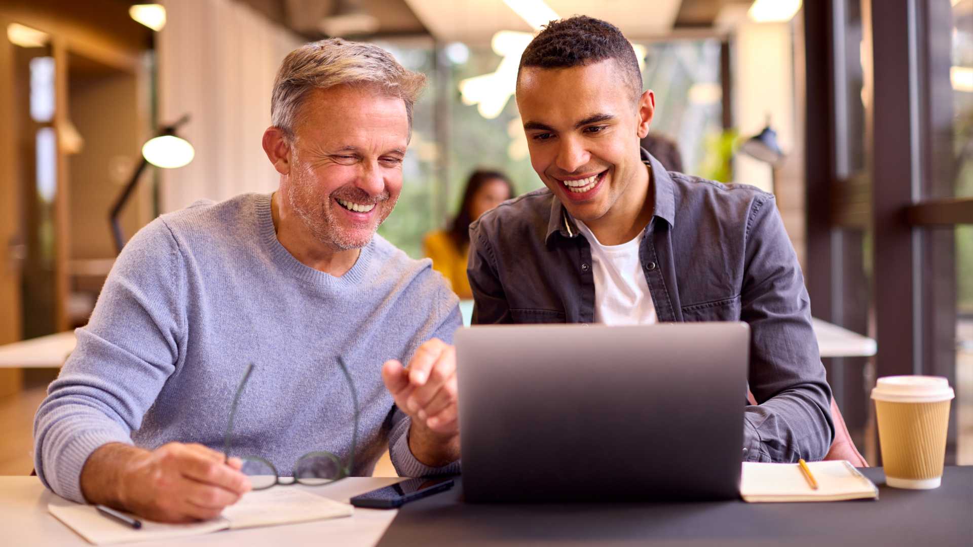 Mature Businessman Mentoring Younger Colleague Working On Laptop At Desk