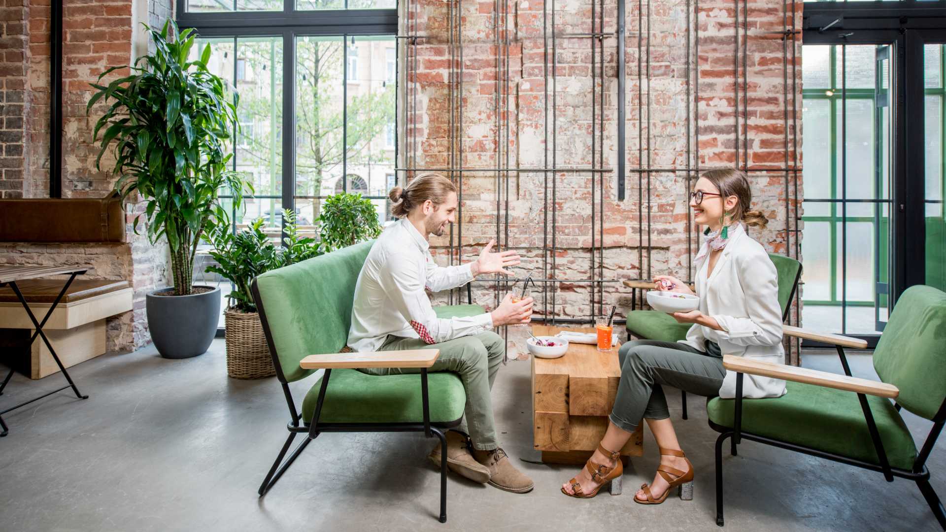 Two business professionals have a conversation over lunch in an open office setting