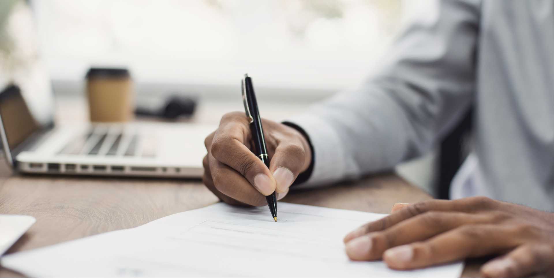 A man holding a pen signs a document in a business setting