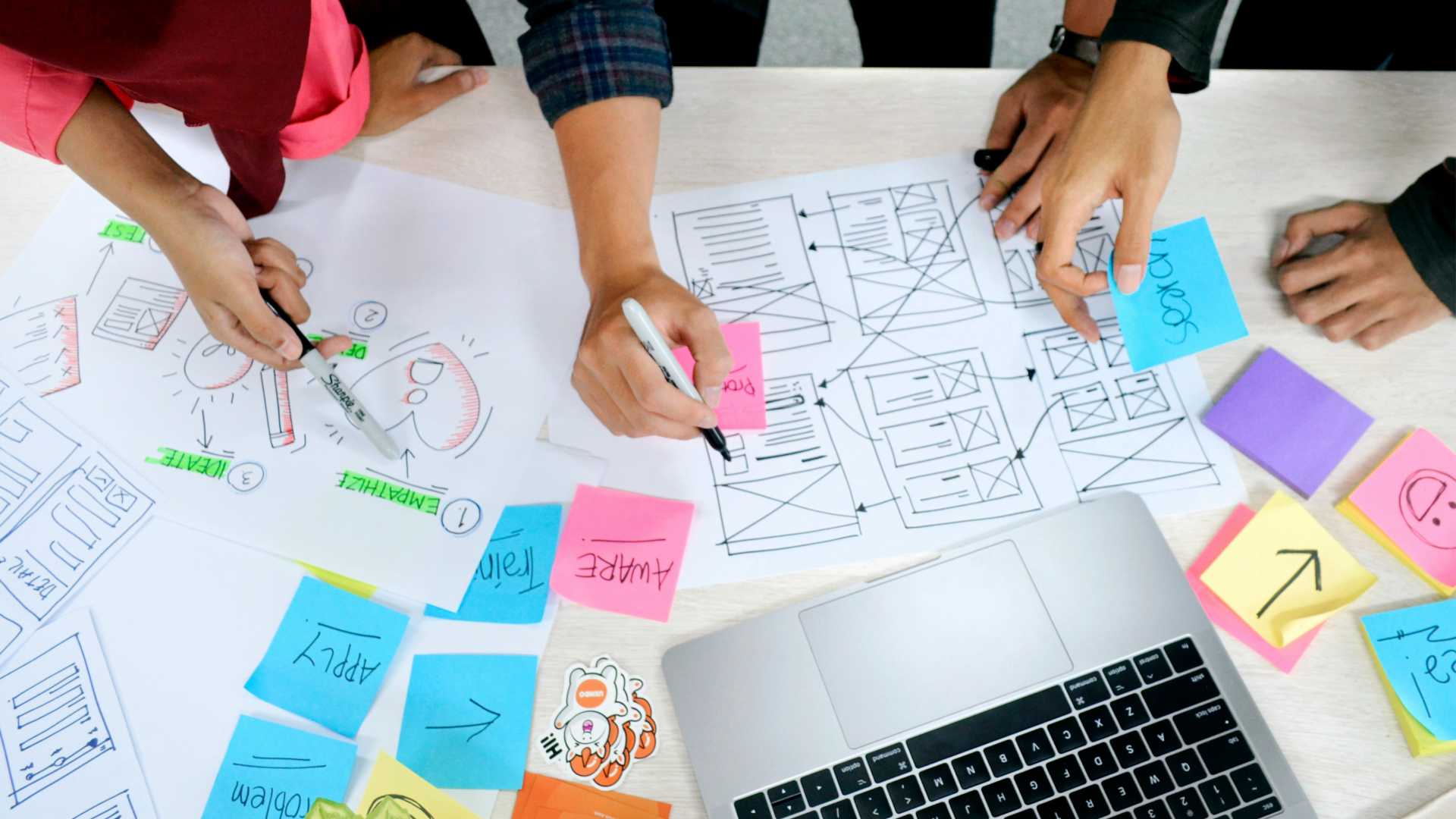 A diverse team collaborates on a laptop, surrounded by colorful sticky notes, fostering creativity and productivity.