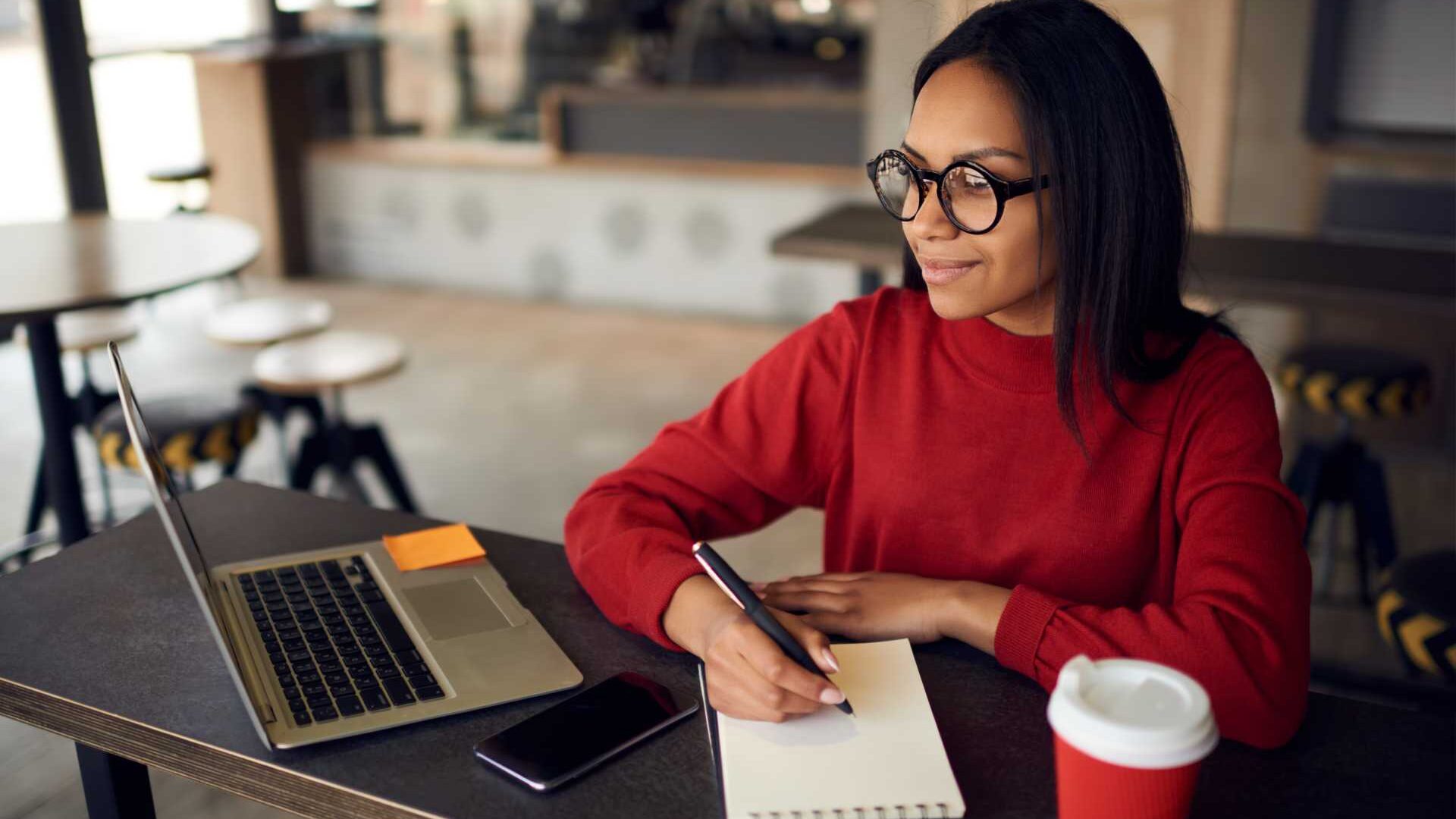 A woman seated in front of an open laptop taking notes