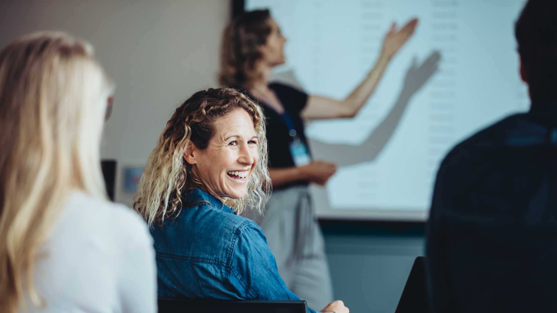 Three training participants sitting in an instructor-led training program with cohorts, one of the trainees is smiling at a another participant because of employee engagement.