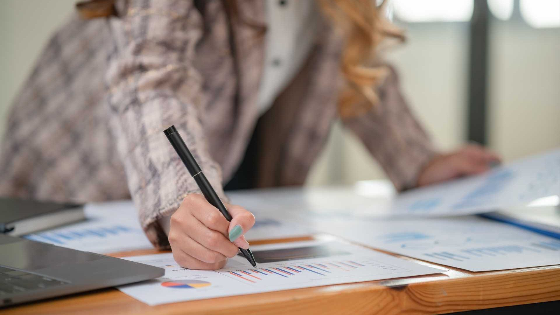 A woman holding a pen overlooking business papers with charts and graphs