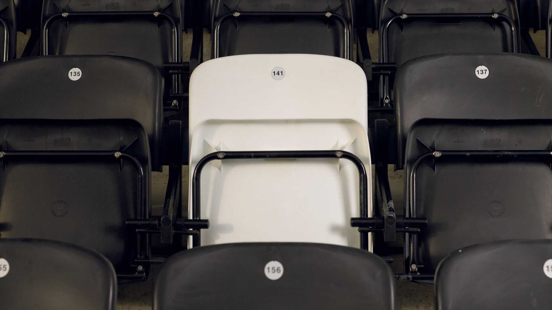 A white stadium seat against rows of black stadium seats